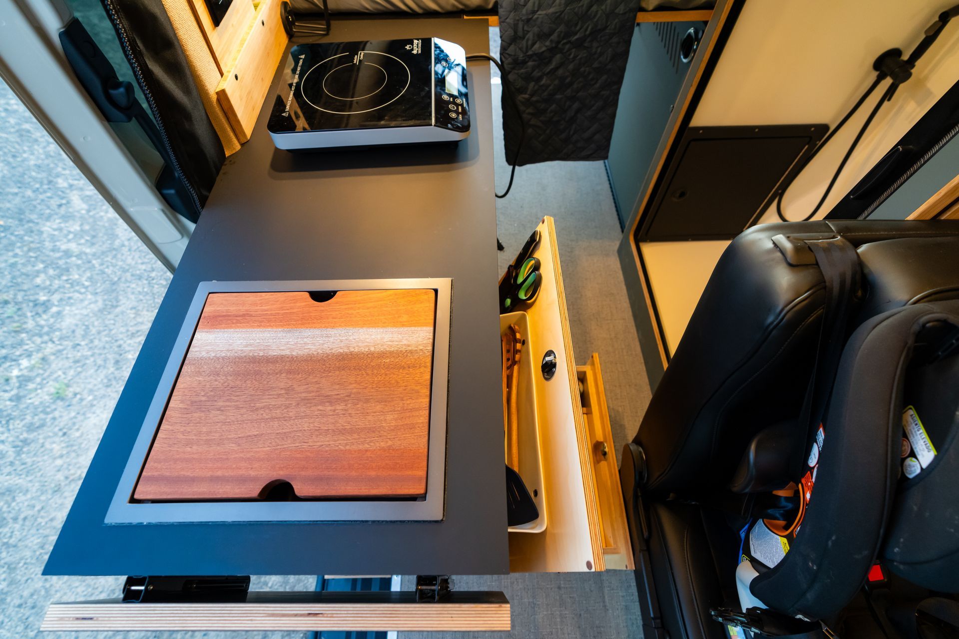 Compact camper van interior with a wood tabletop, black seat, and kitchen sink area