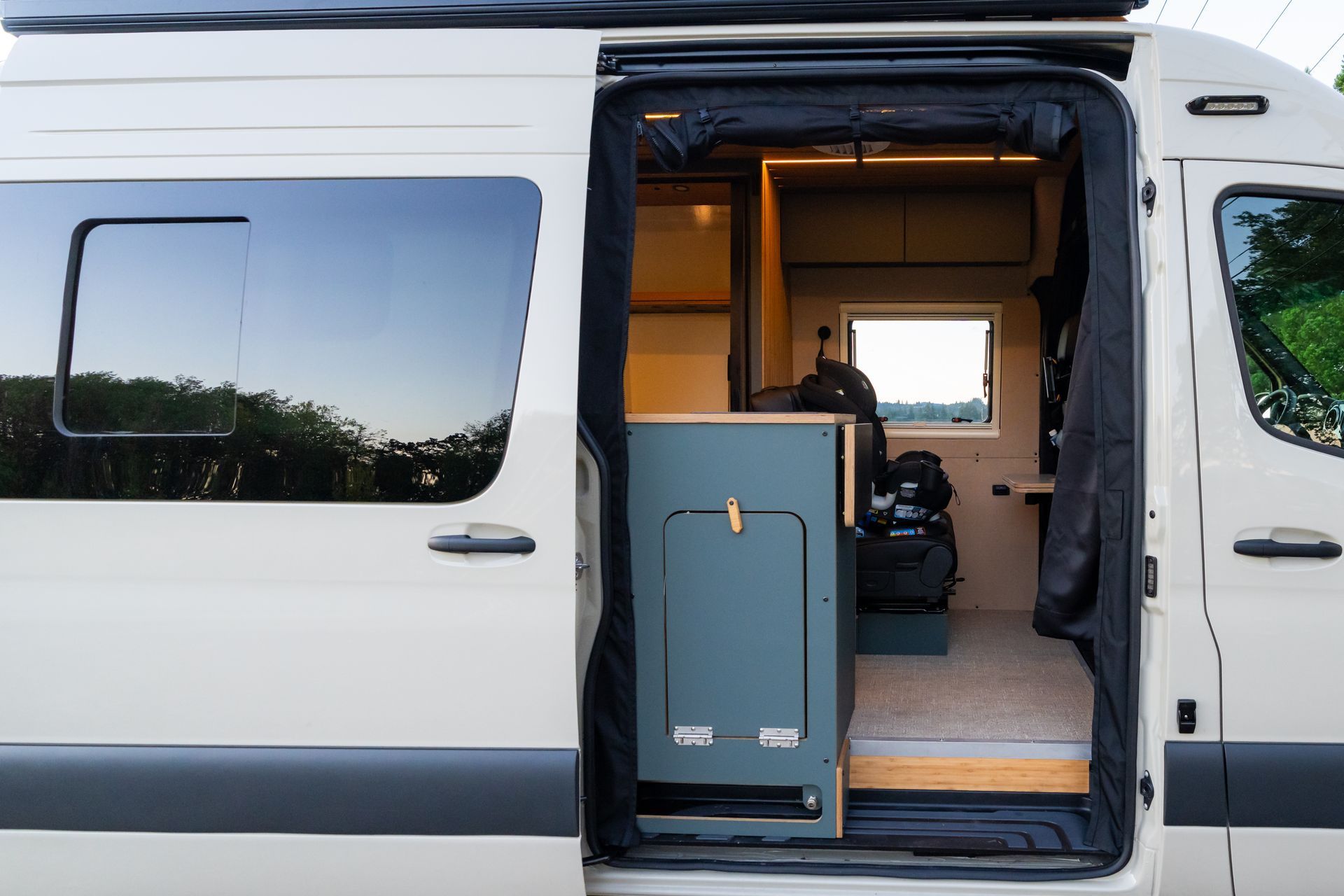 Open camper van side door showing a compact interior with a blue cabinet and wooden floor