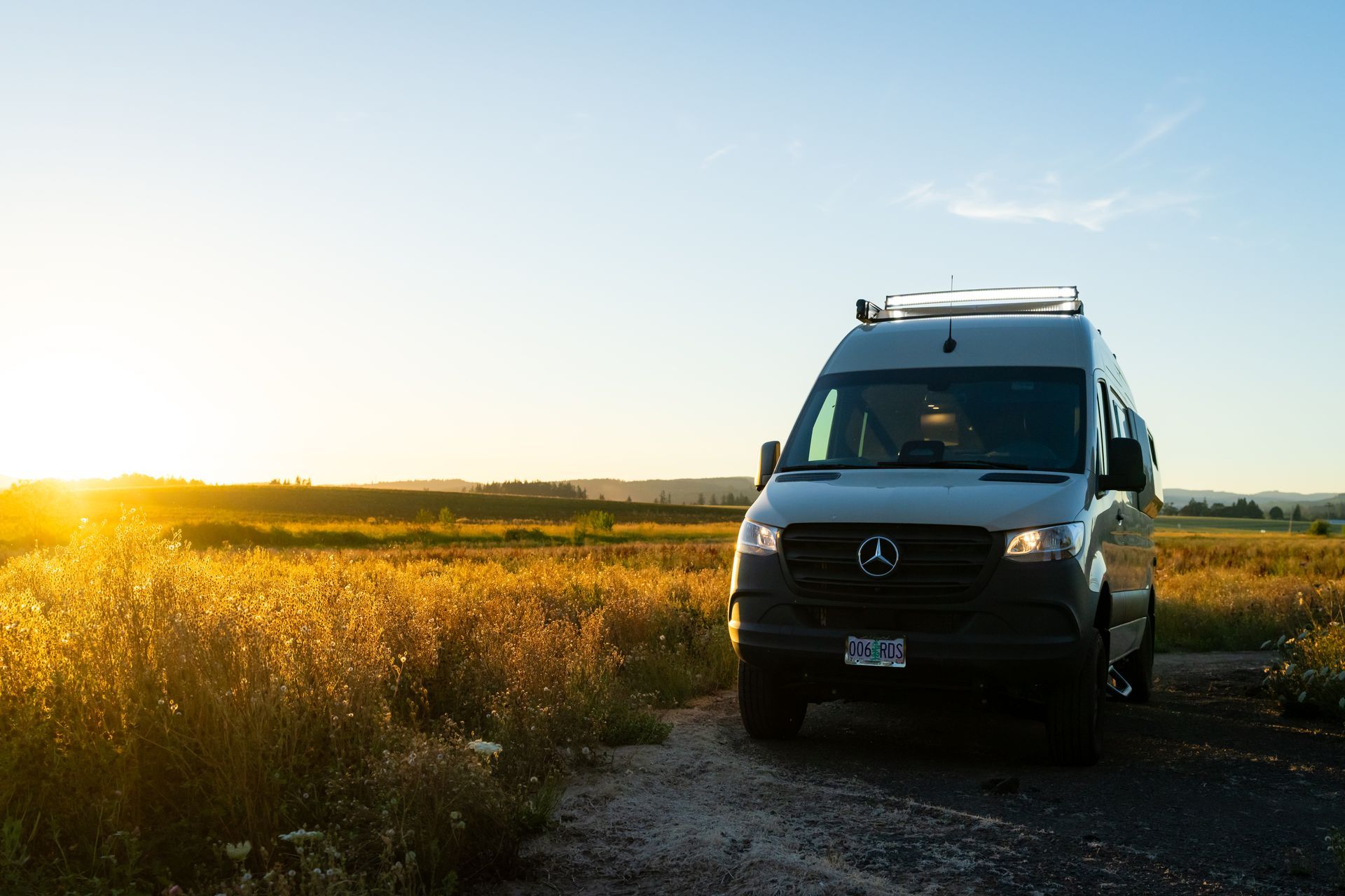 White van parked on a dirt road beside a golden field at sunset