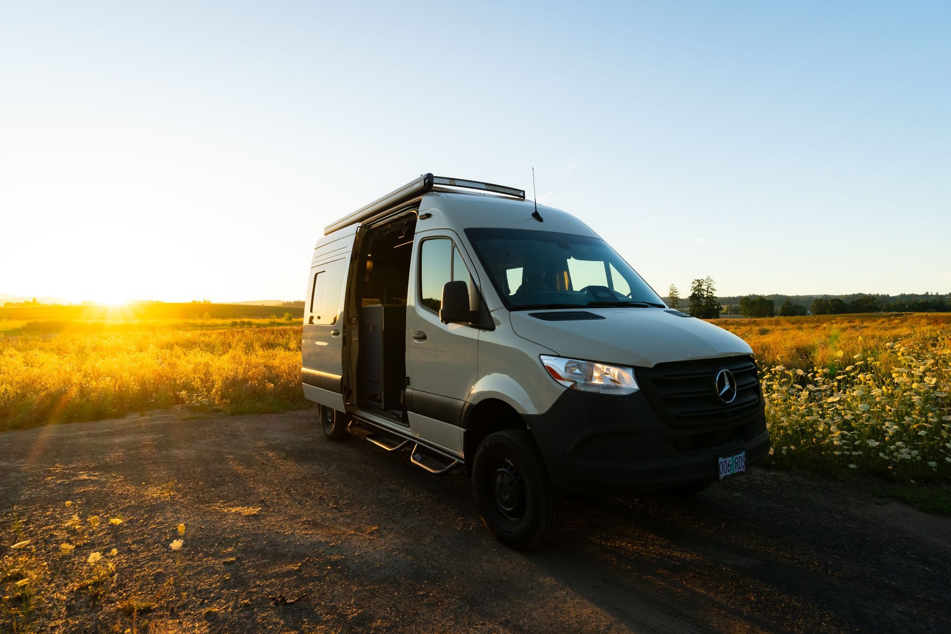 White van parked on a dirt road at sunset beside a field of yellow flowers