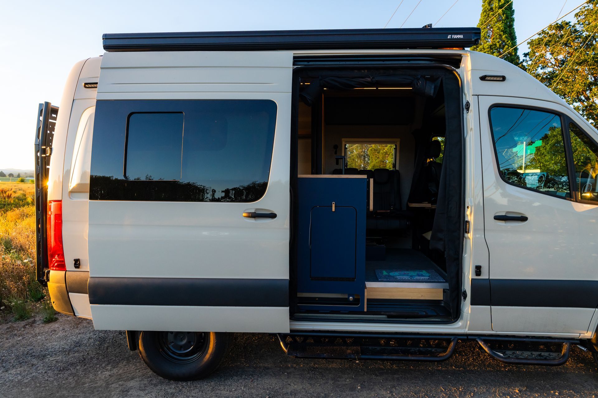 White camper van with sliding side door open, revealing blue interior at sunset.