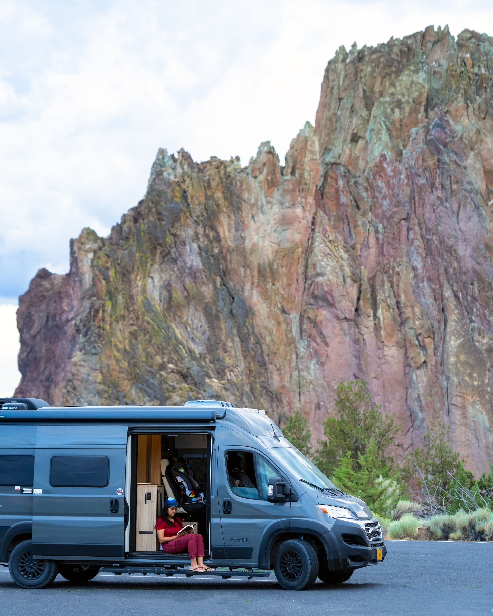 Gray camper van parked beside a towering rocky cliff in a scenic outdoor setting