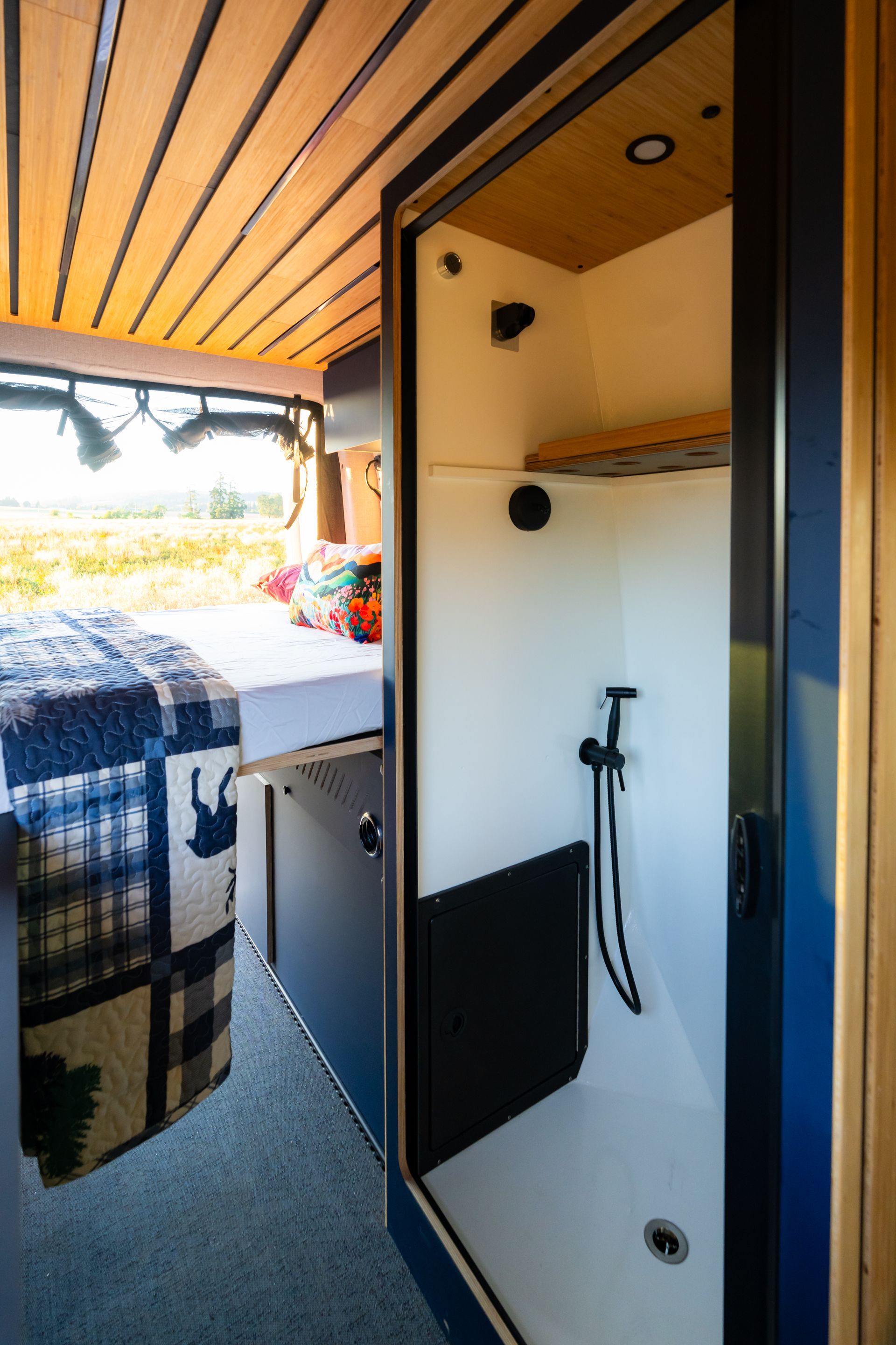 Compact camper van shower stall with white walls, black trim, and a mounted showerhead and hose