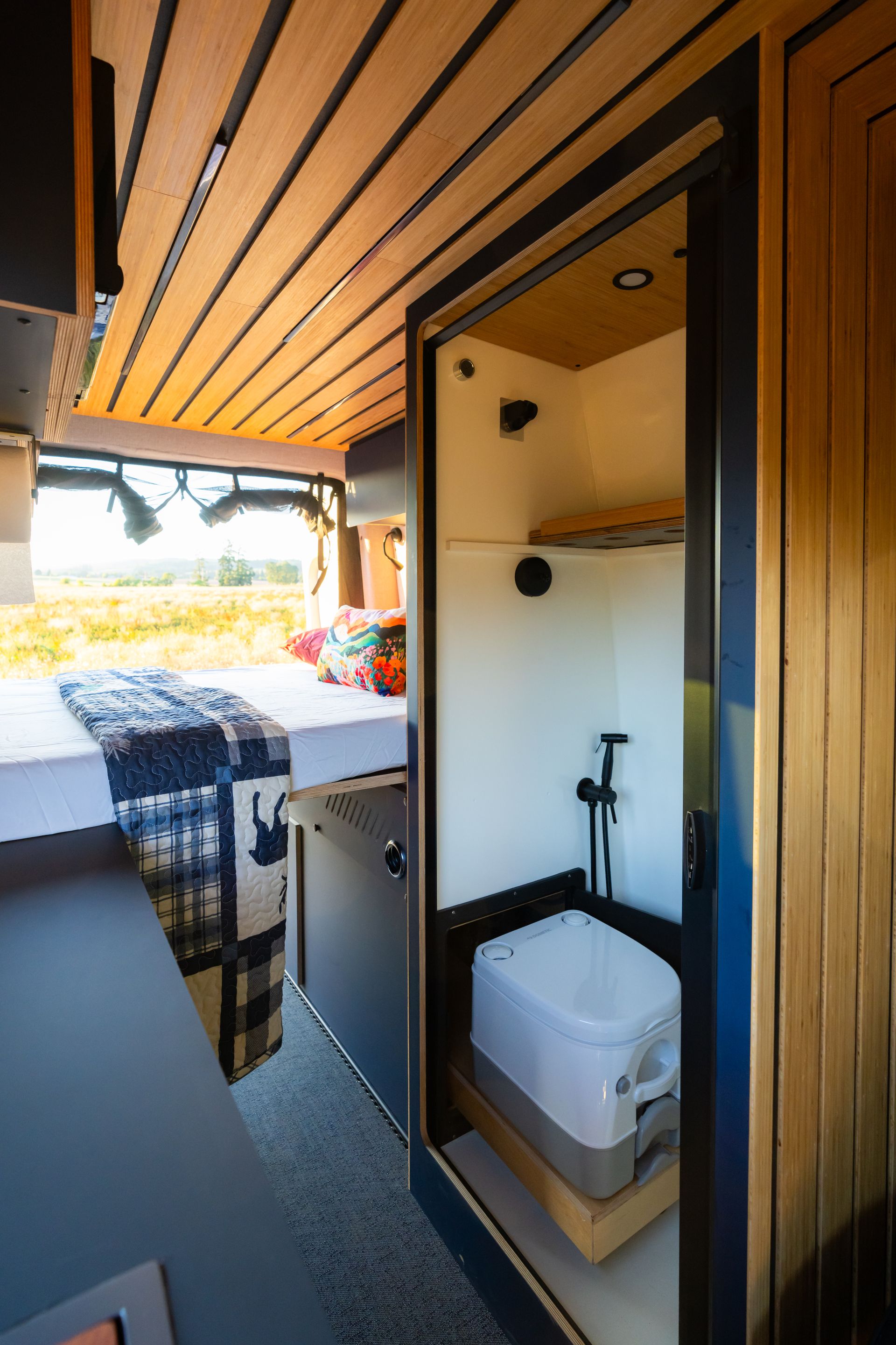 Compact camper van interior with built-in bathroom, toilet, shower, and bed by the open rear door