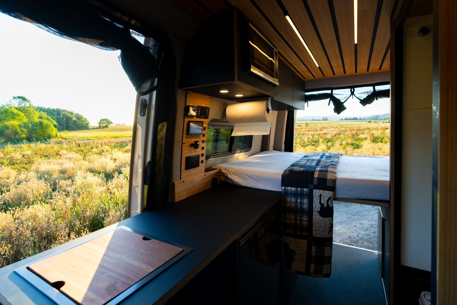 Modern van interior with bed, desk, and open view of grassy landscape at sunset