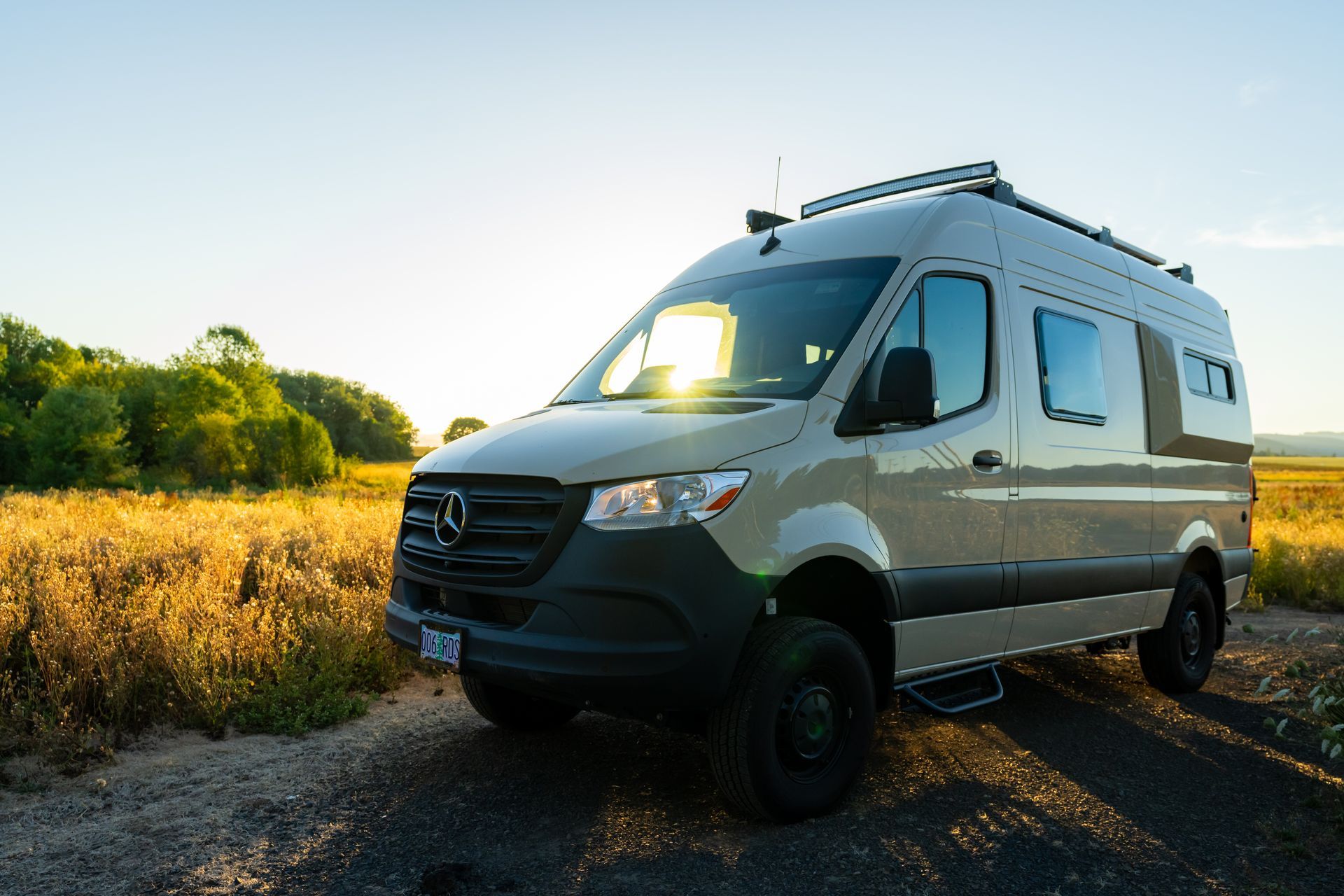 White camper van parked on a gravel road beside golden fields at sunset