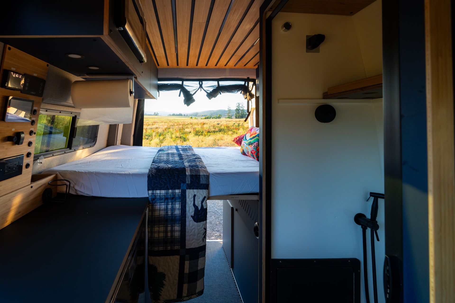 Compact camper van interior with open rear doors overlooking a sunny beach and ocean.