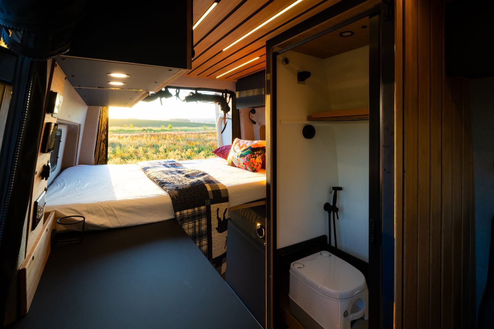 Compact RV interior with dinette, front cab seats, and overhead storage in gray and wood tones