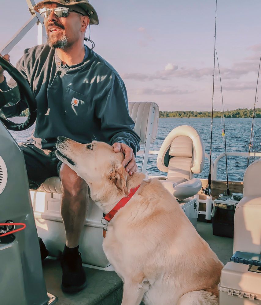 A man driving a boat with a dog sitting next to him