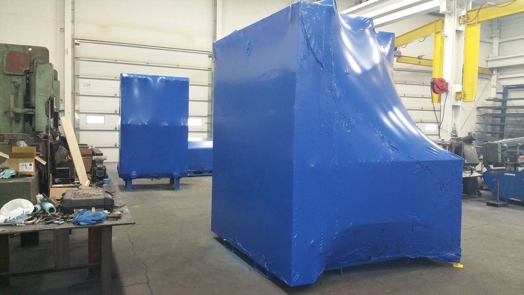 A large blue box is wrapped in plastic in a factory