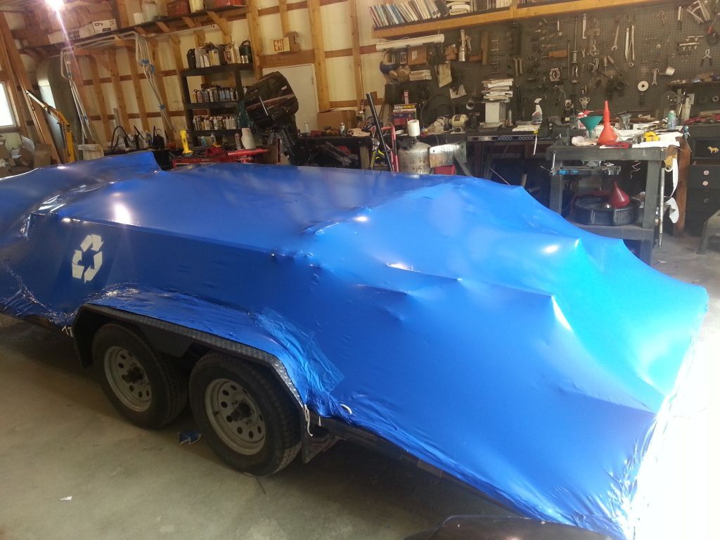 A blue trailer is wrapped in blue plastic in a garage