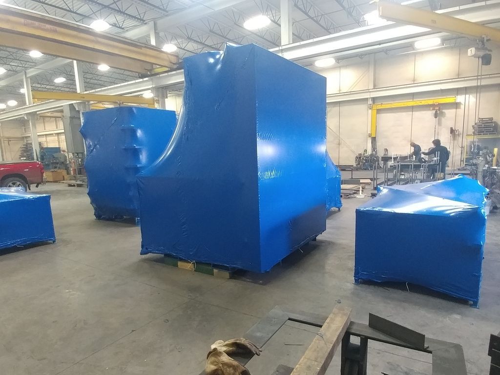 A large blue object is wrapped in plastic in a factory