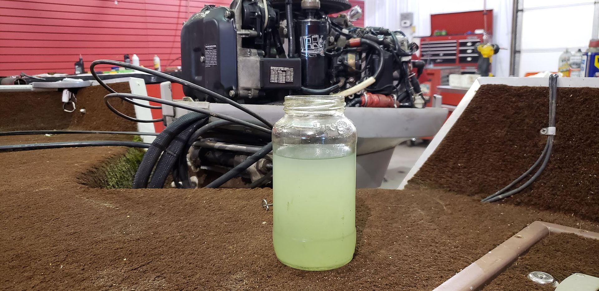 A bottle of liquid is sitting on a table in front of a boat engine.