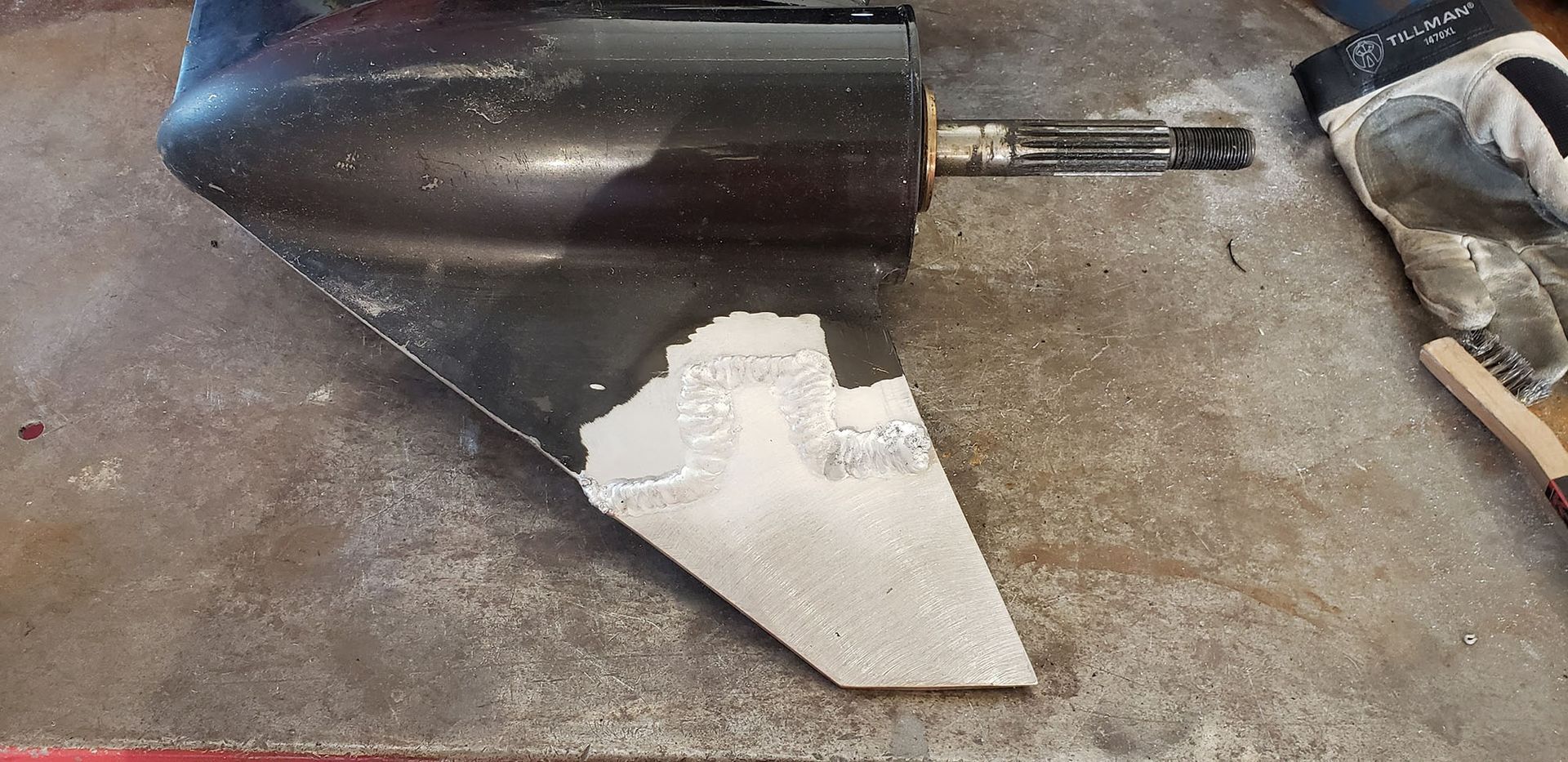 A boat propeller is sitting on a table next to a brush and gloves.