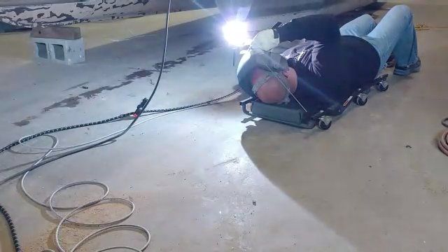A man is laying on the floor welding a piece of metal.