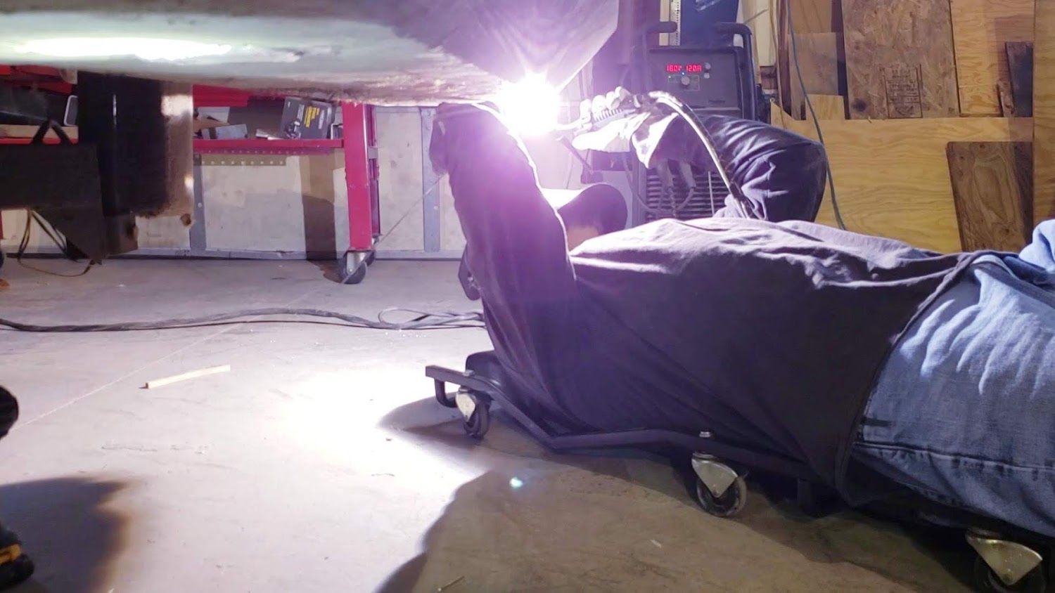 A man is welding under a car in a garage