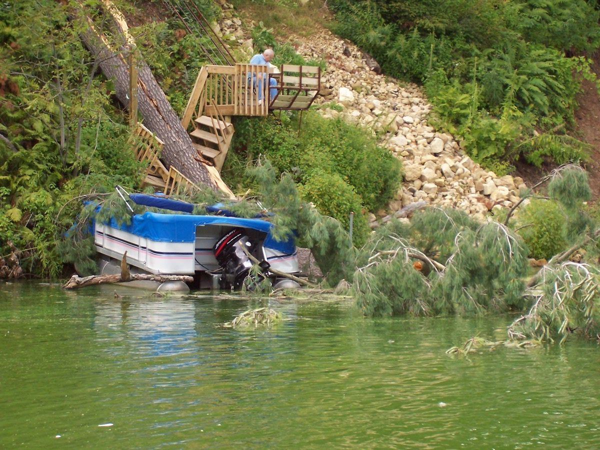 Large tree fallen onto a pontoon boat along the shoreline of Lake Menomin in Menomonie Wisconsin after a summer storm with boat recovery and repair services by Anchor Marine near Eau Claire