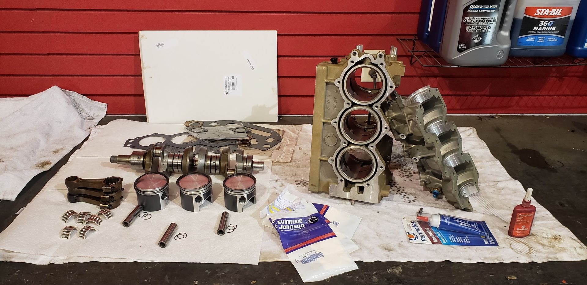 Johnson 70 HP outboard engine components laid out during powerhead rebuild including pistons, crankshaft, bearings, and cylinder block at Anchor Marine boat repair shop in Menomonie Wisconsin serving the Eau Claire area