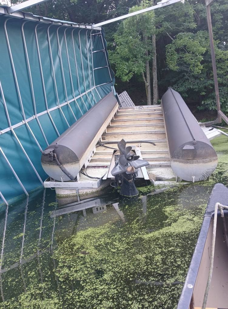 Pontoon boat flipped upside down in a damaged boat lift after a summer storm on a Wisconsin lake dock near Eau Claire and Menomonie with storm damage inspection and repair by Anchor Marine