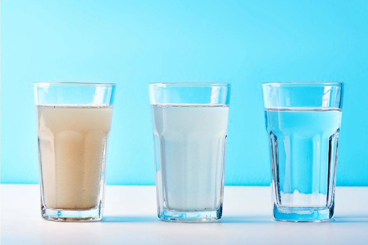 Three glasses of water, one cloudy, one clear, and one blue-tinted, on a white surface