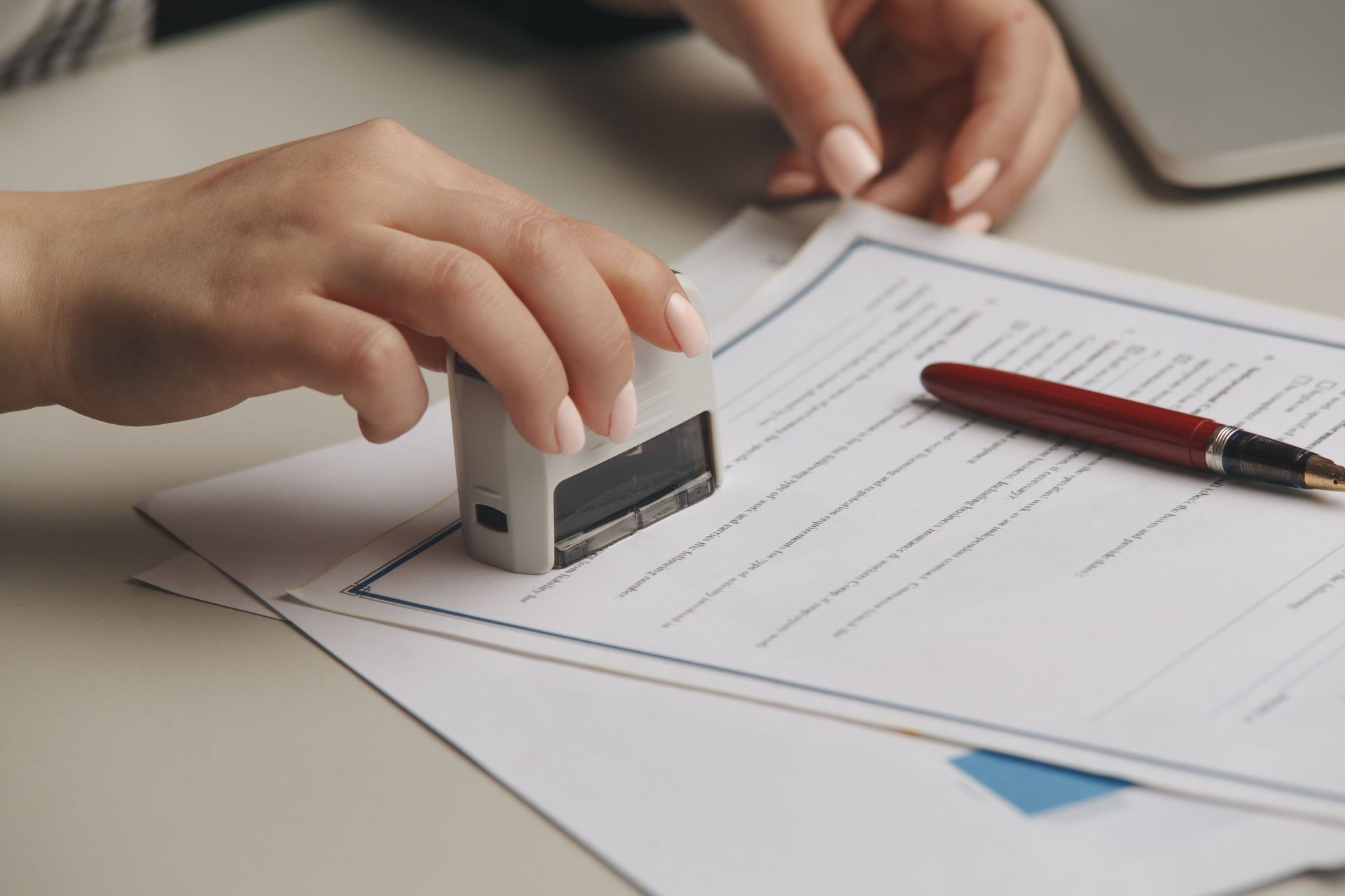 Hands stamping a document beside a red pen on a desk