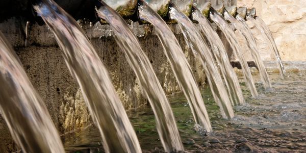 Water pours from a row of stone spouts into a shallow fountain pool.