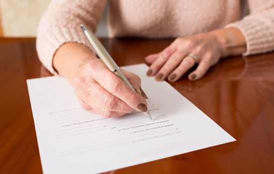 A woman is writing on a piece of paper with a pen.