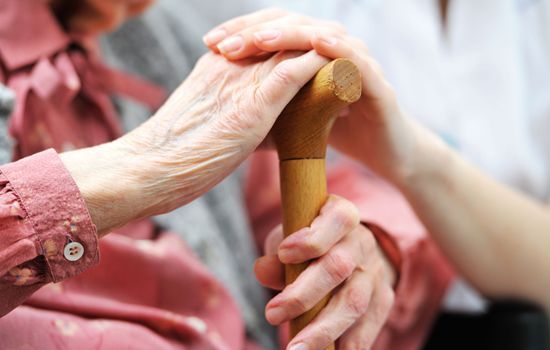 A woman is holding the hand of an older woman who is holding a cane.