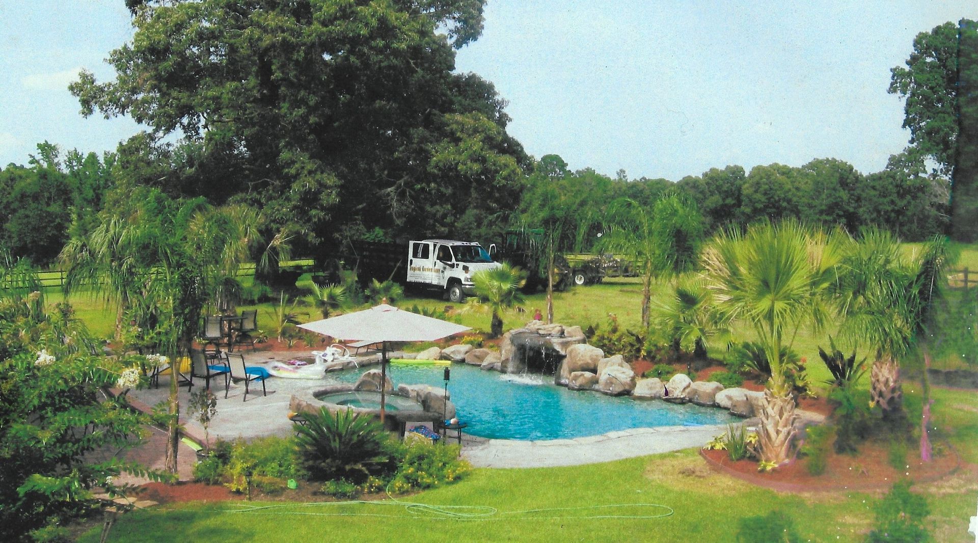 Backyard pool with waterfall, palm trees, and a large grassy area.