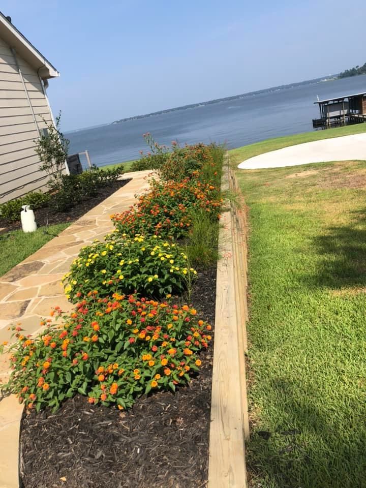 Stone path lined with colorful flowering bushes and a lake view.