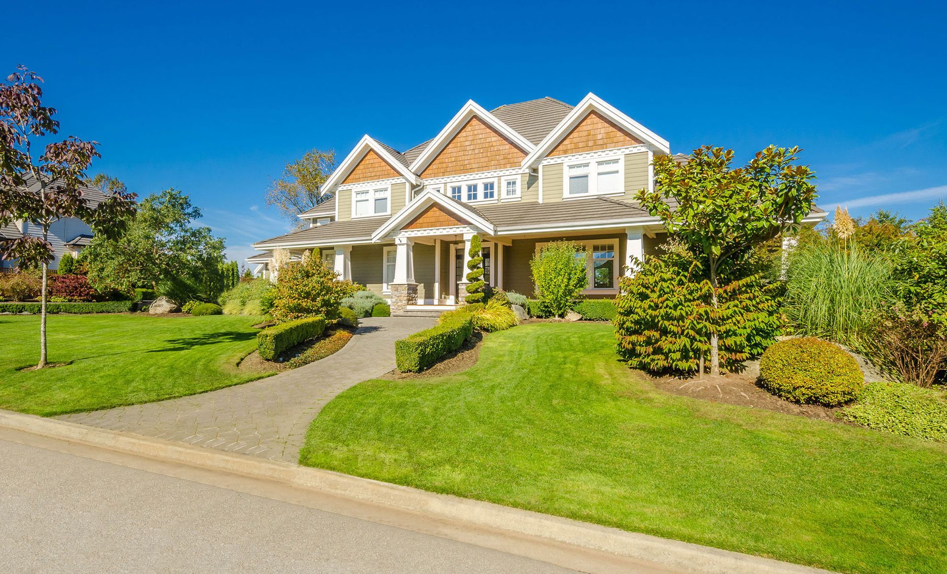 Two-story house with green lawn, path, and landscaping under a clear blue sky.