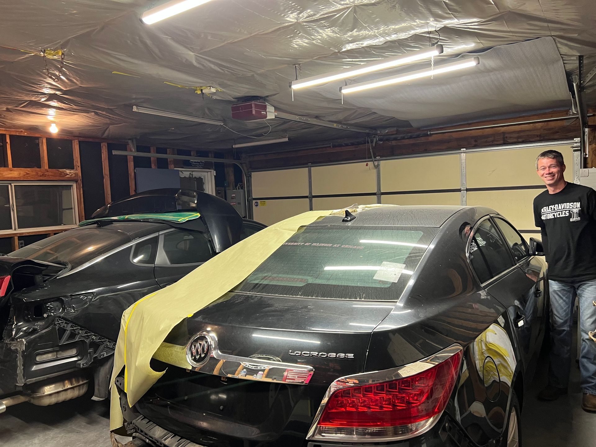 A man is standing next to a wrecked car in a garage.