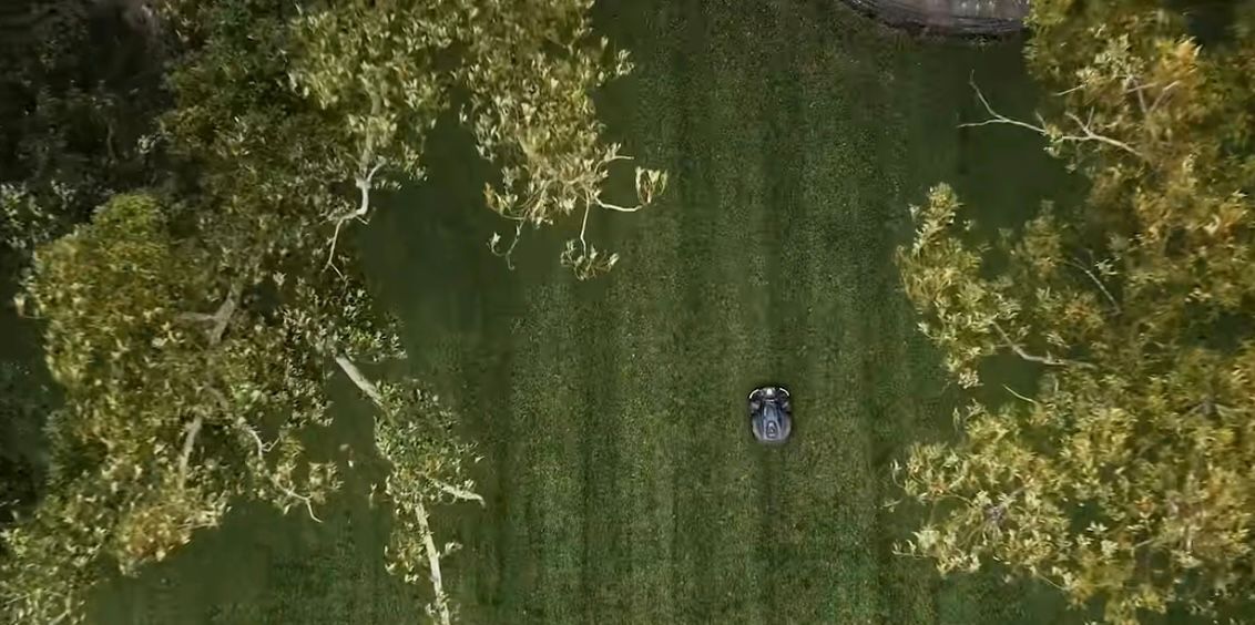 Aerial view of a lawn mower cutting grass between two trees.