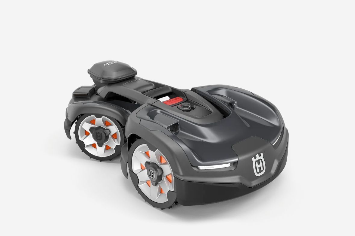Black Husqvarna robotic lawnmower on a white background, with orange accents on the wheels.