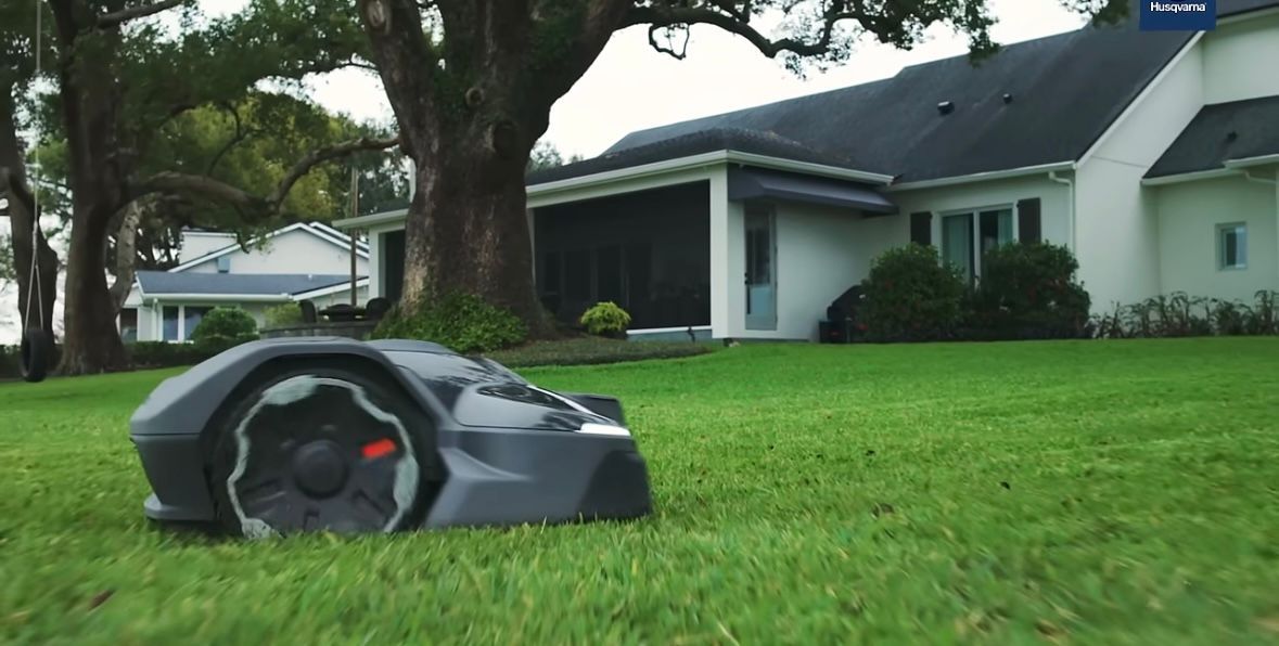 Robotic lawnmower on a green lawn in front of a white house with a dark roof.