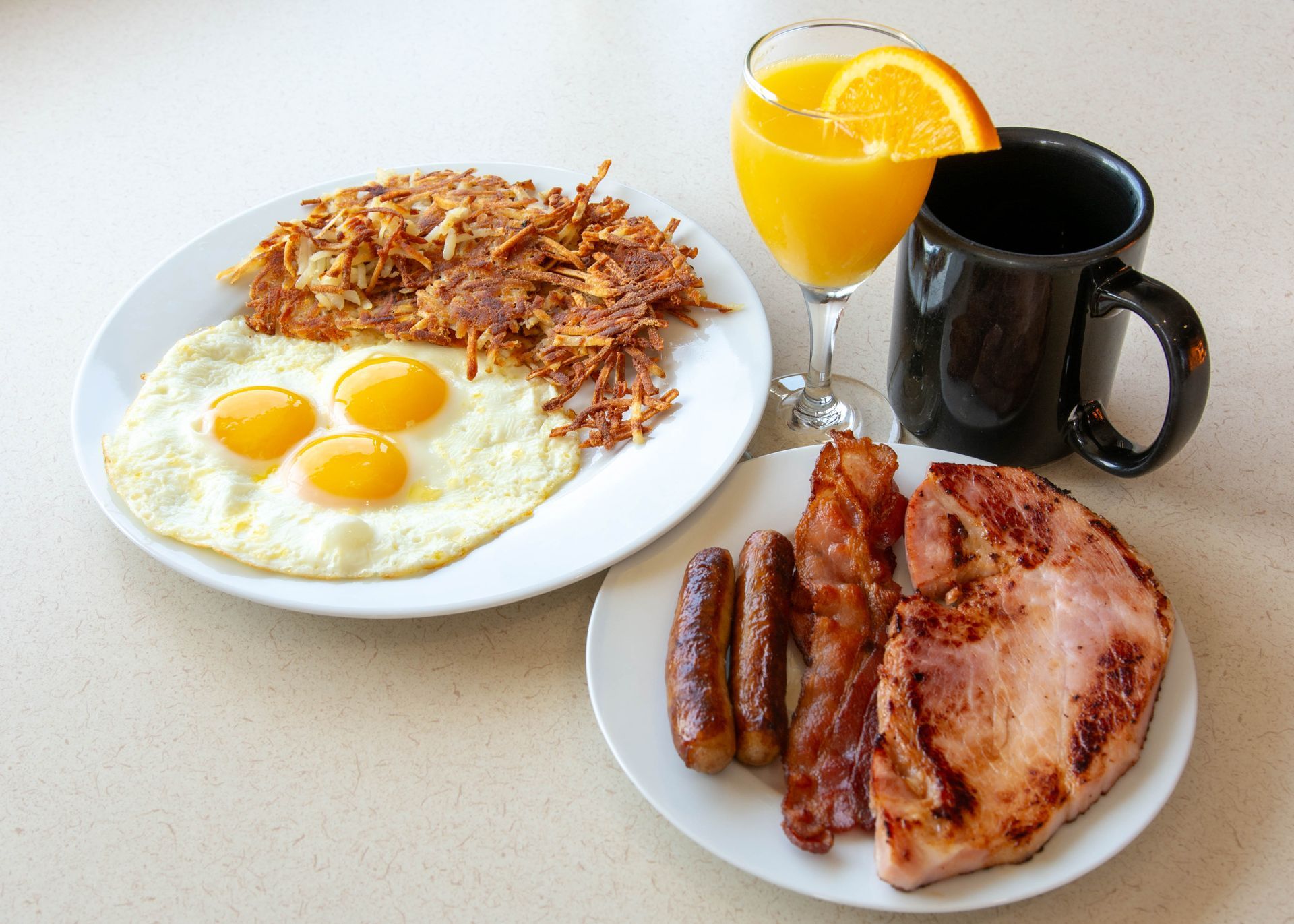 Breakfast plate with eggs, hash browns, sausage, steak, orange juice, and coffee on a table
