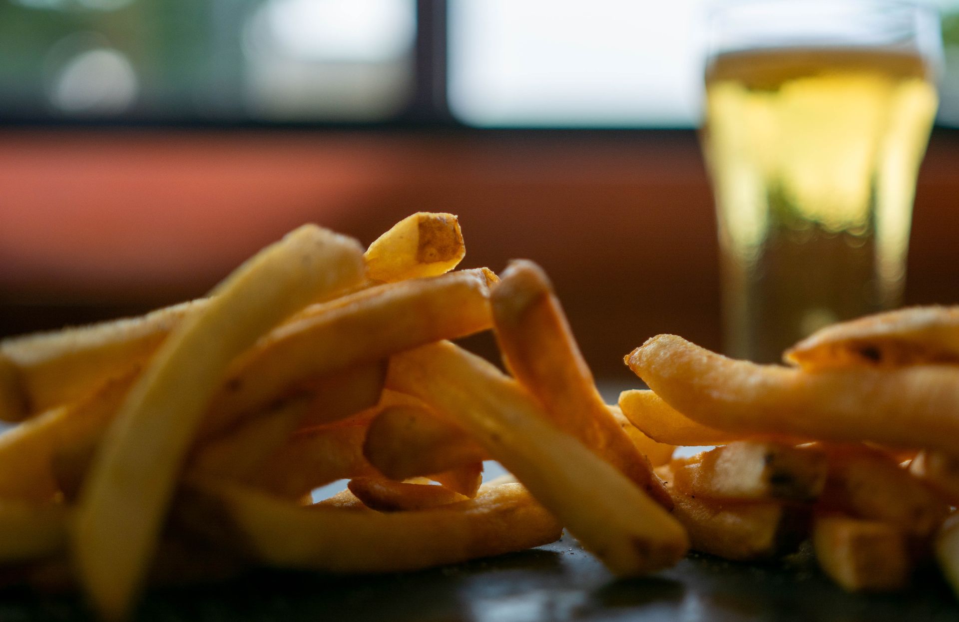 Golden French fries on a plate in a dim restaurant, with a blurred drink in the background