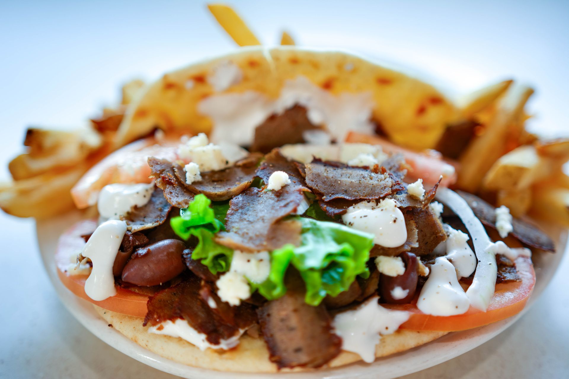 Taco with shredded beef, lettuce, and sour cream on a plate, with fries in the background