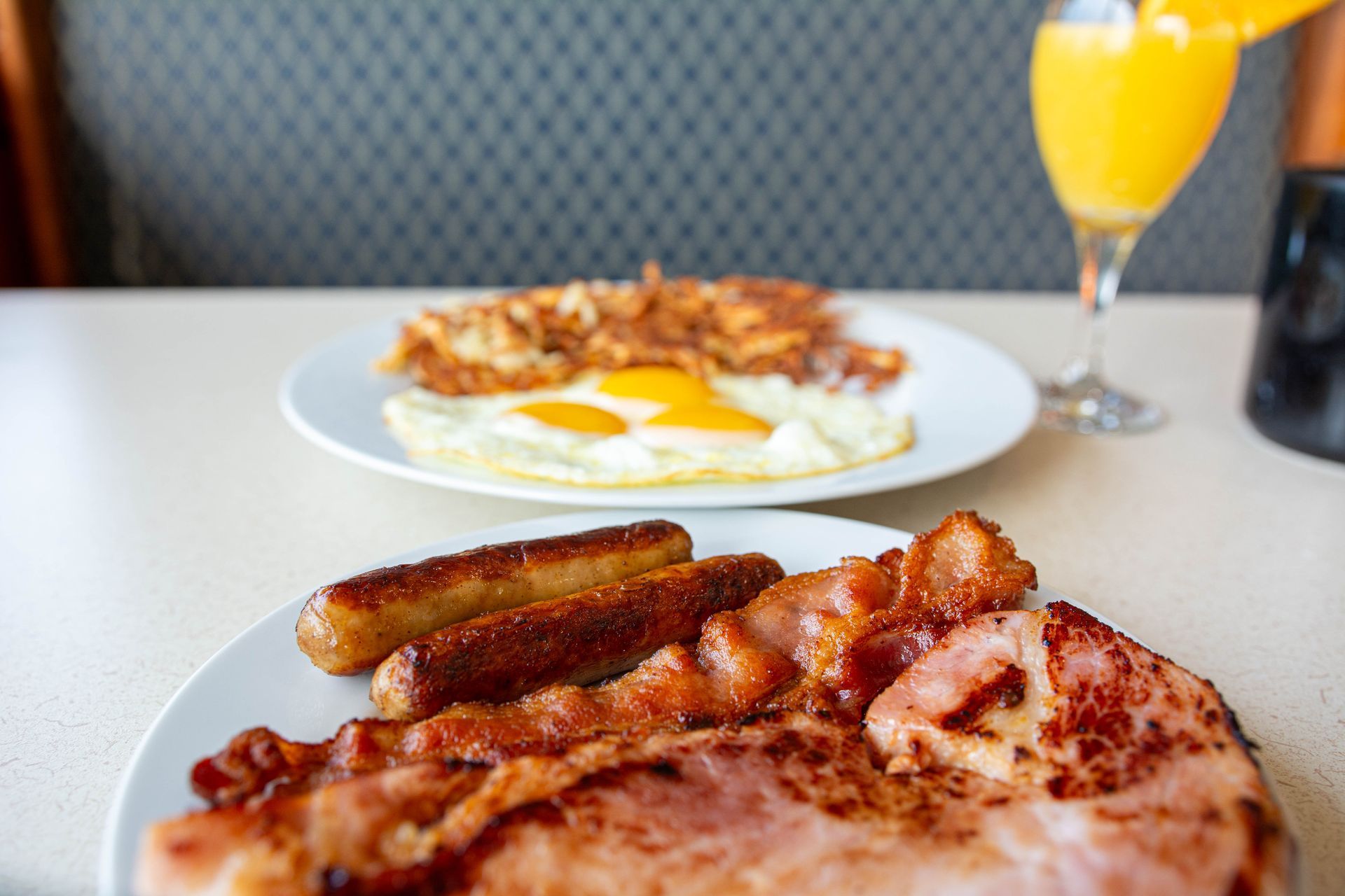 Plate of steak, roasted potatoes, bacon, and eggs on a table with a drink in the background