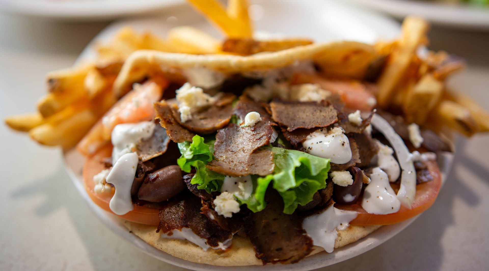 A bowl of fries topped with meat, greens, and sauce on a table
