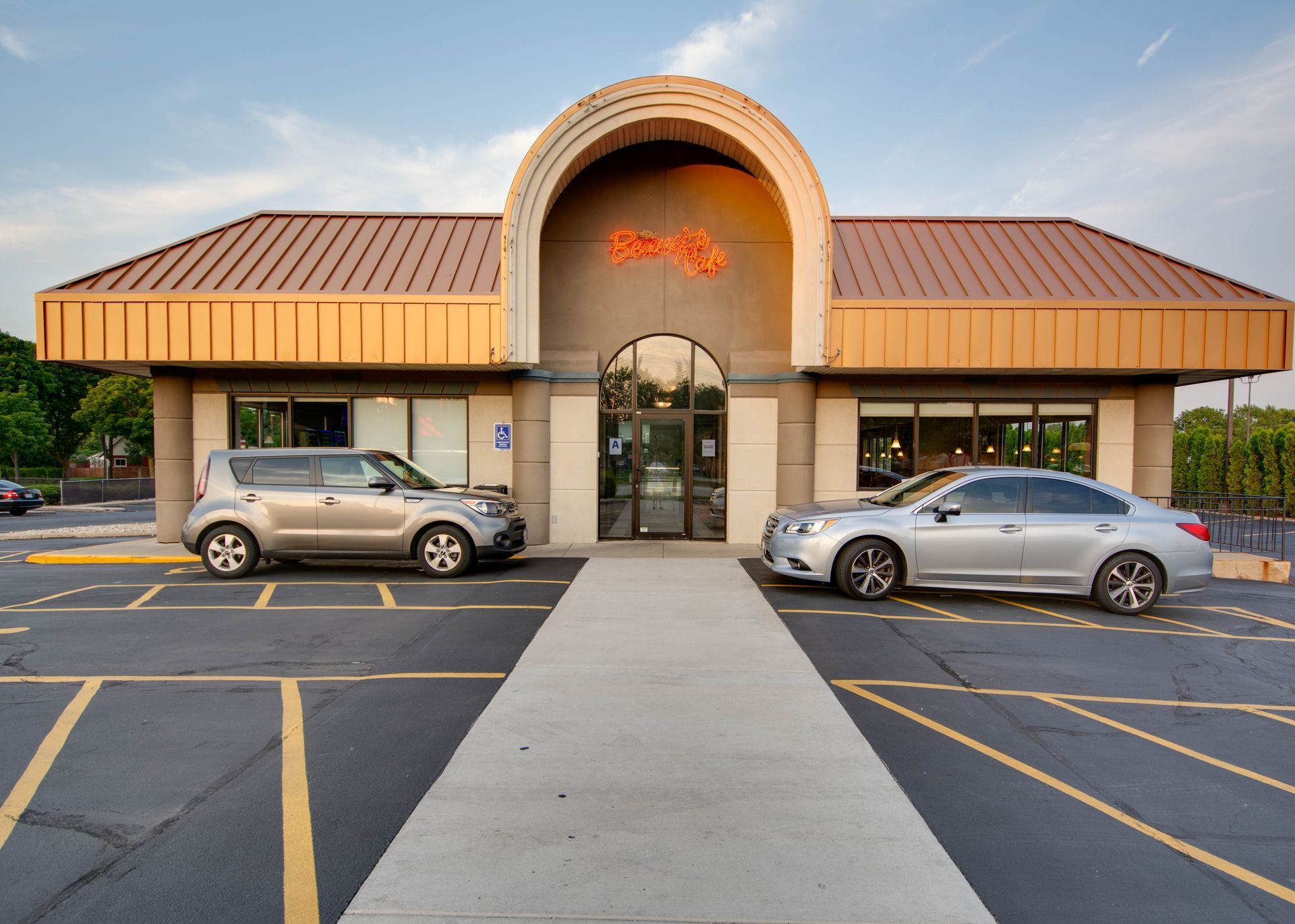 Front view of a tan commercial building with two parked cars and a walkway leading to the entrance