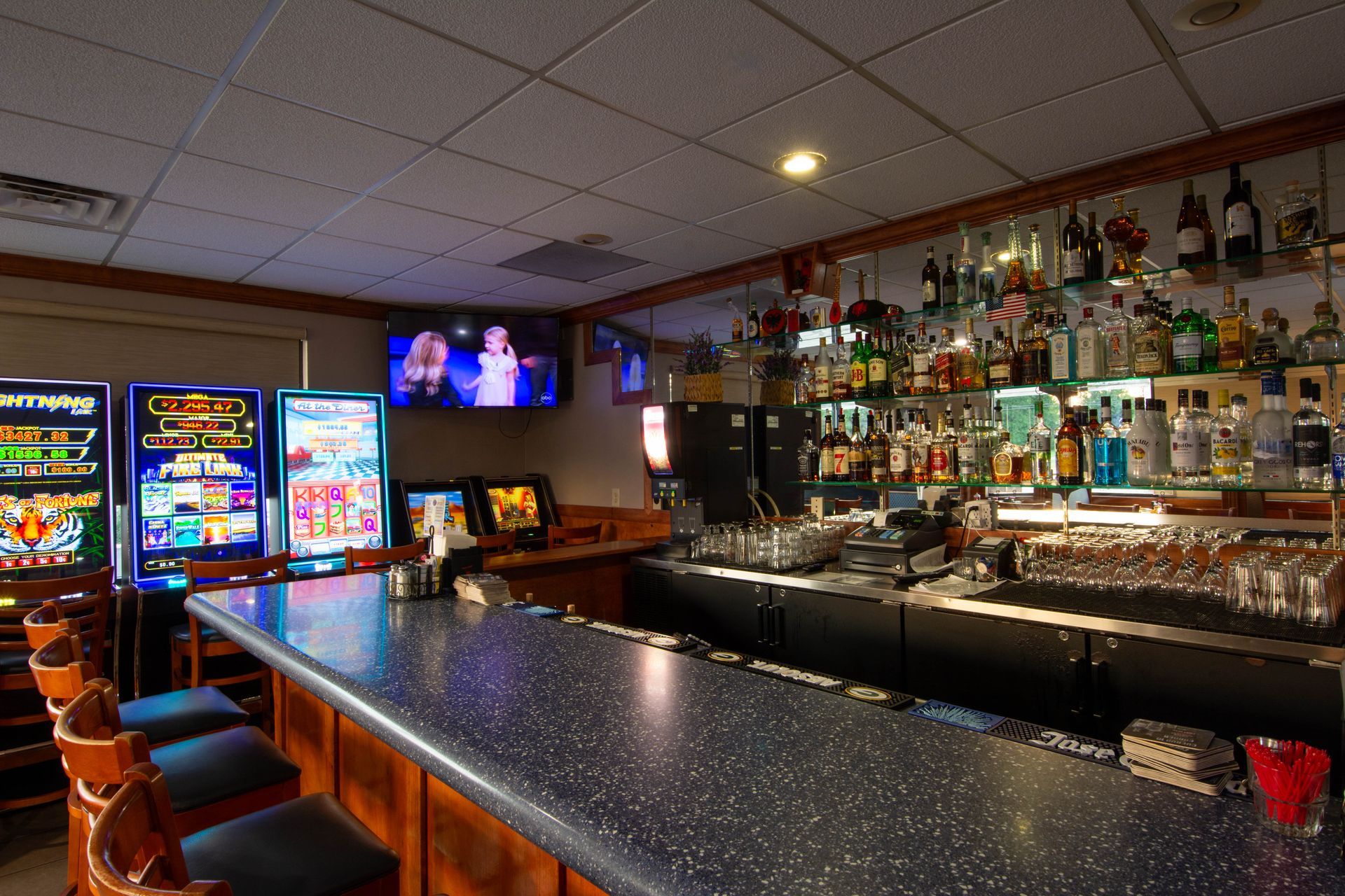 Bar with illuminated slot machines, mirrored liquor shelves, and a long countertop in a dimly lit lounge