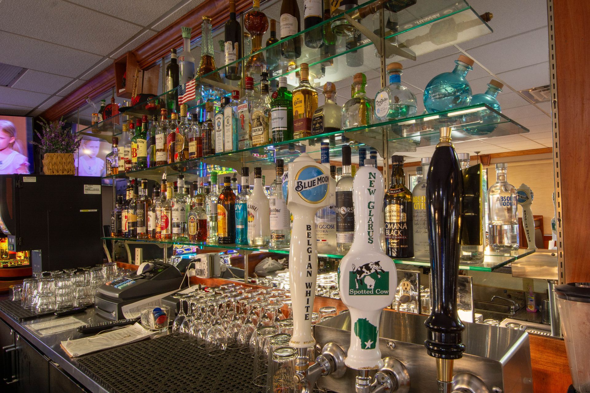 Colorful bar interior with shelves of liquor bottles and glassware behind the counter