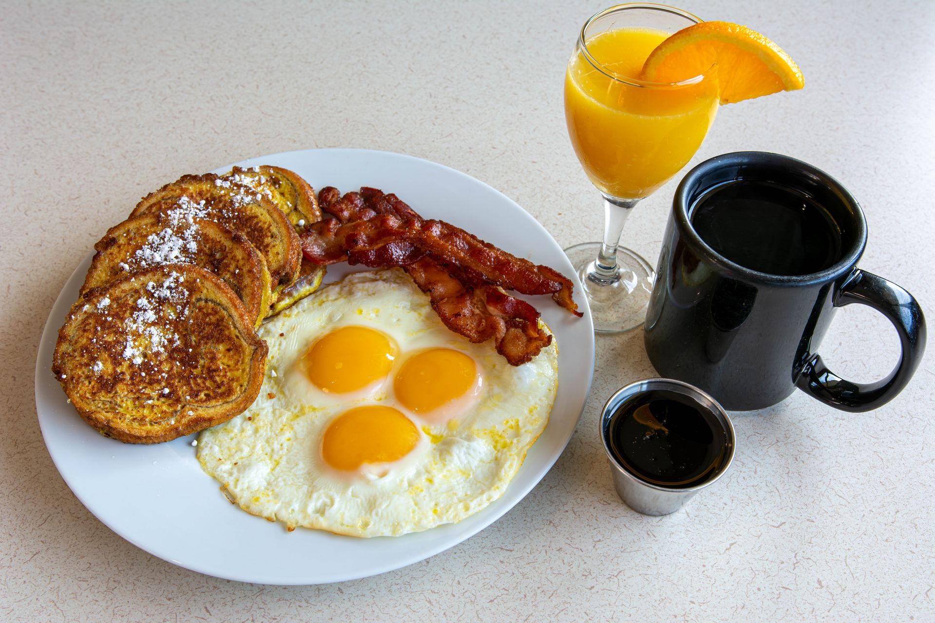 Breakfast plate with pancakes, eggs, bacon, coffee, and orange juice on a table