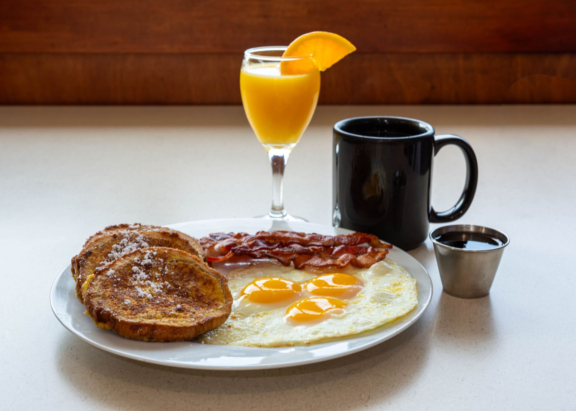 Breakfast plate with eggs, bacon, toast, coffee, and orange juice on a table