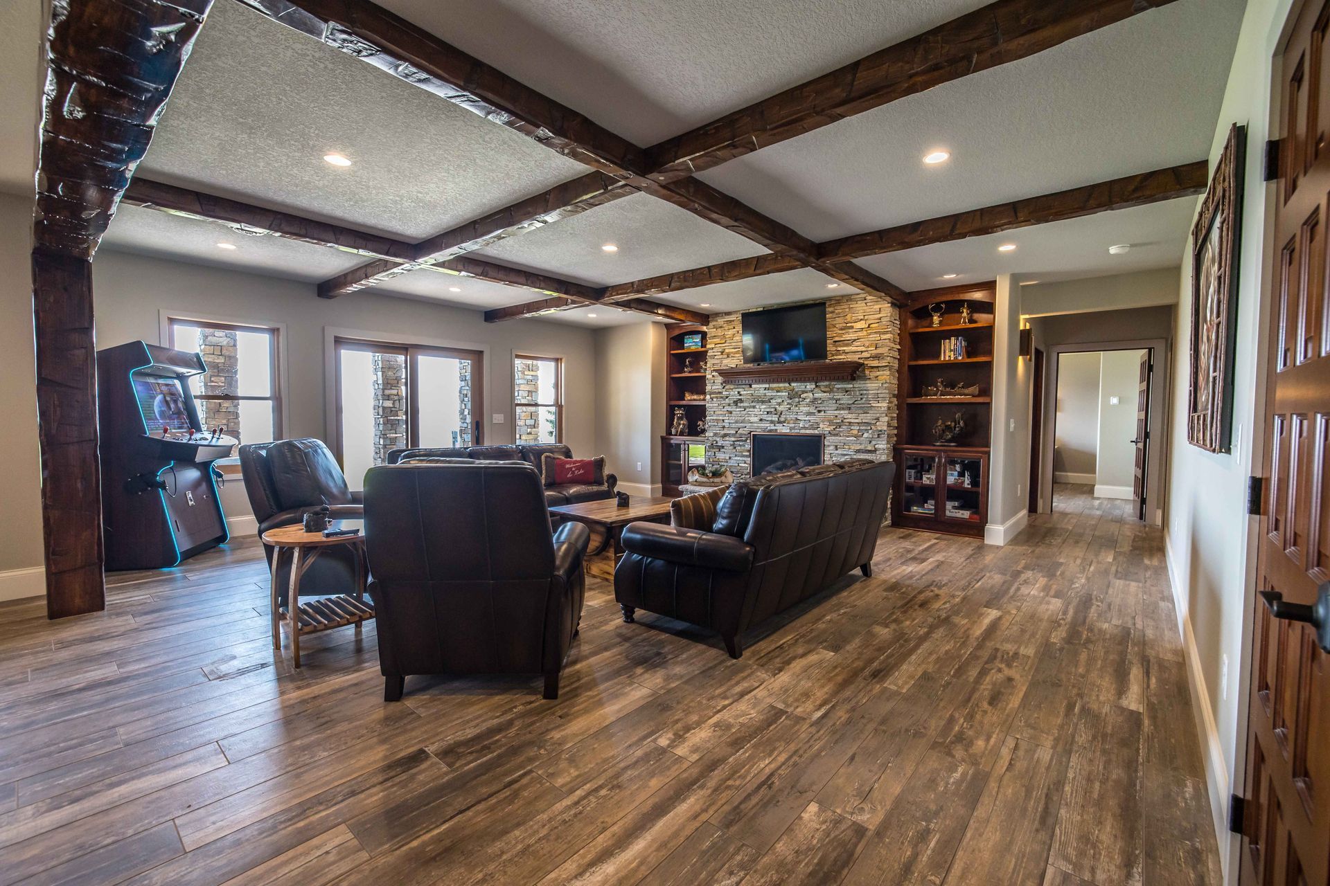 Living room with wood beams, fireplace, arcade game, leather furniture, and hardwood floors.