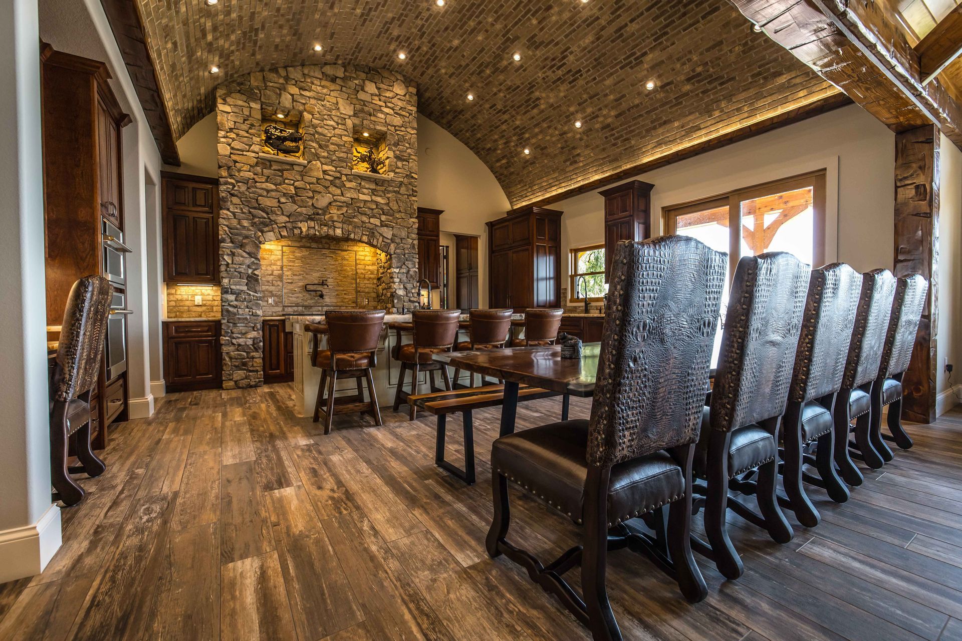 Rustic dining room with a long wooden table, stone fireplace, and high-backed chairs.