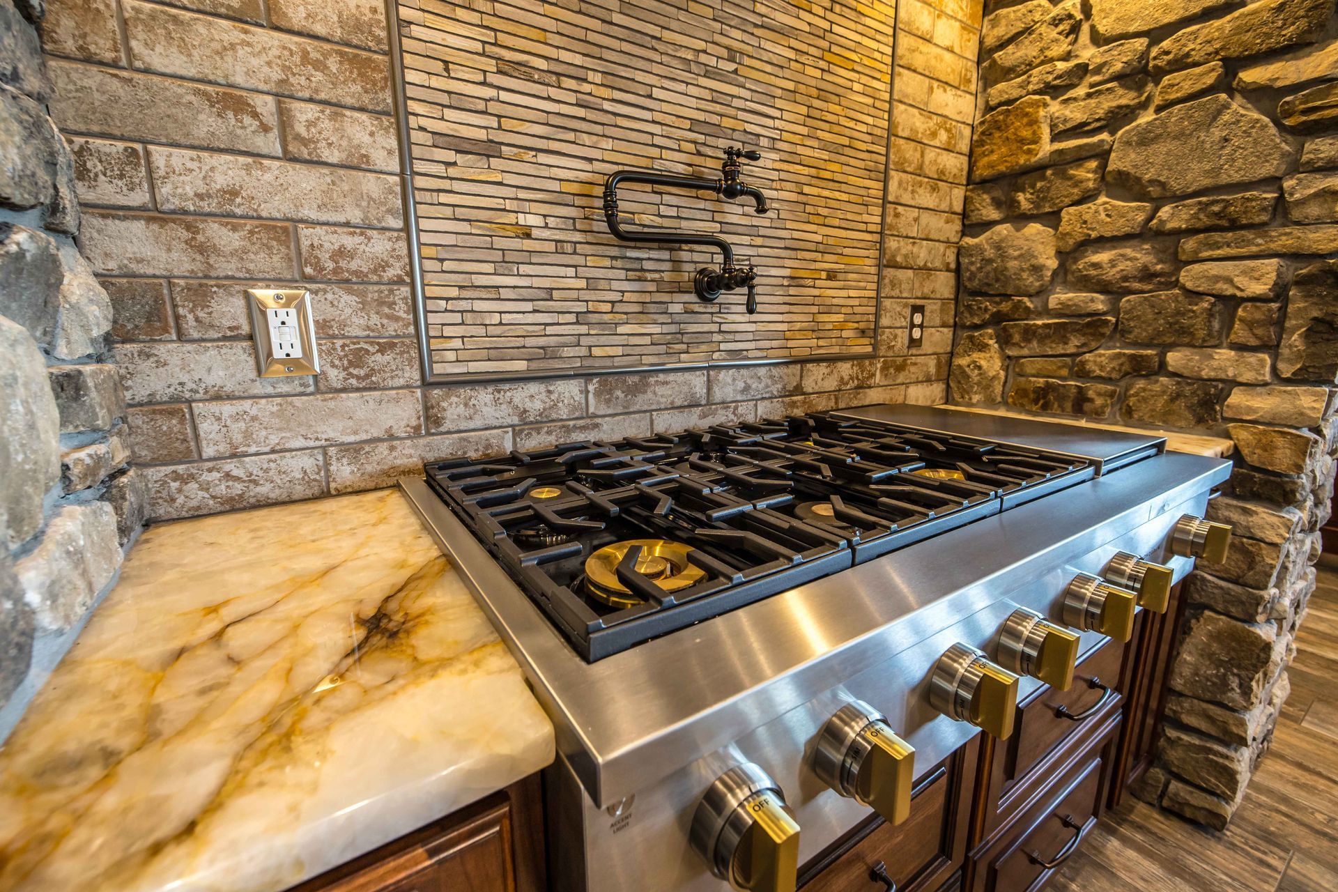 Stainless steel stovetop in a kitchen with stone walls and marble countertops.