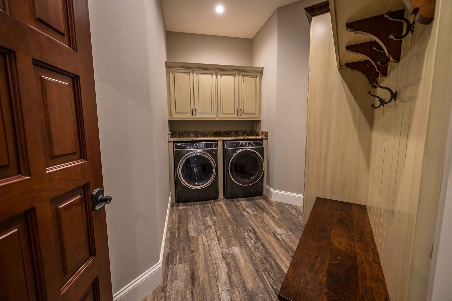 Laundry room with washer, dryer, cabinets, and wooden bench.