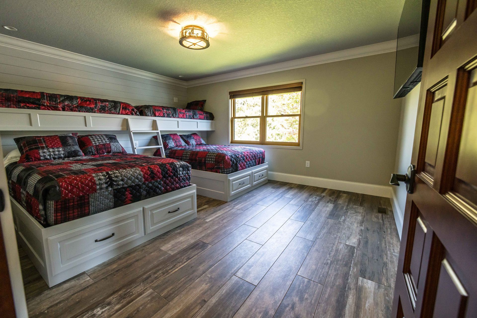 Bedroom with bunk beds, a double bed, and wooden flooring. Red and black patterned bedding.